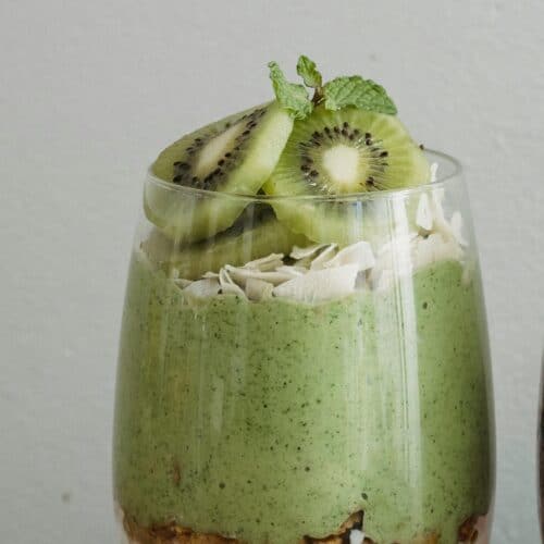 Copo de café da manhã com camadas de iogurte, granola, creme de kiwi com maracujá e fatias de kiwi por cima